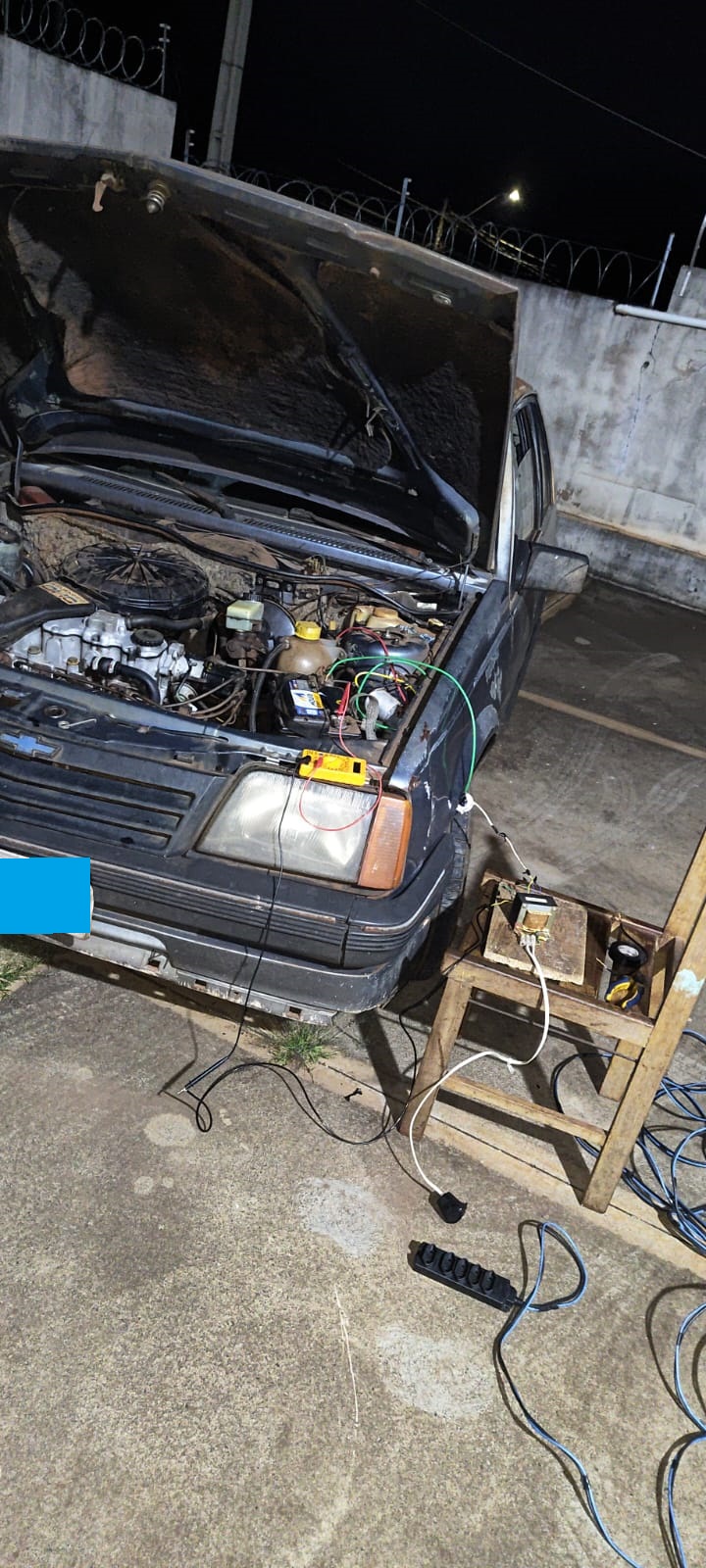 Monza com o capô aberto e o primeiro carregador improvisado ao lado
