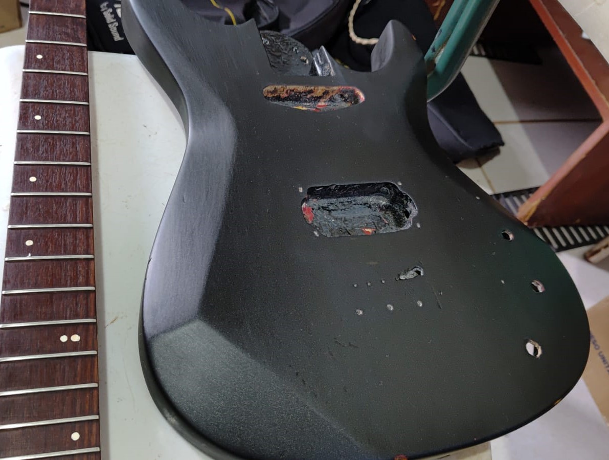 Corpo e braço da guitarra desmontados, com cavidades e marcas das modificações expostas