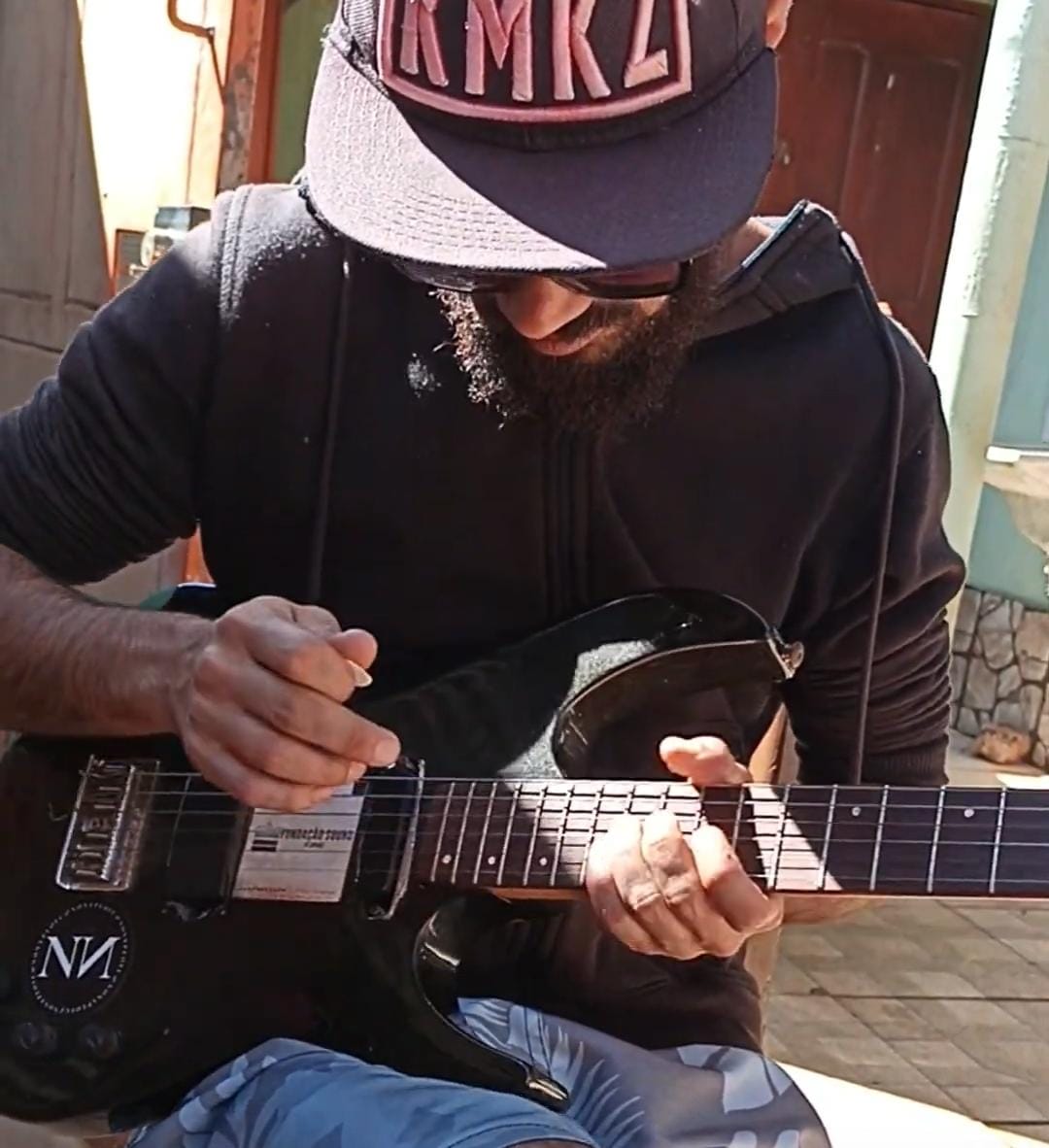 Marcos tocando a guitarra preta já modificada com adesivos