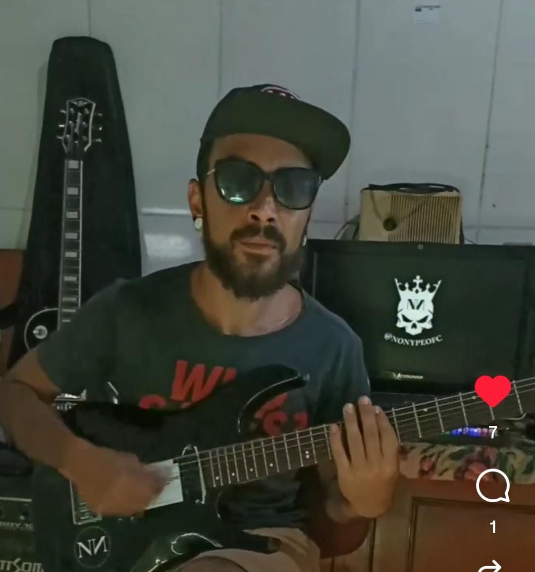 Marcos praticando com a guitarra preta em frente a equipamentos musicais